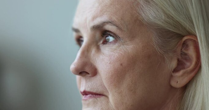Close up side view face of sad, cheerless mature woman staring into distance feels unhappy, suffers from loneliness, mental disorder, senile disease. Marriage split, personal life or health concerns