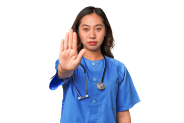 A young nurse chinese woman standing with outstretched hand showing stop sign, preventing you.