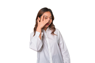 A young chinese woman blink at the camera through fingers, embarrassed covering face.