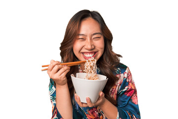 Happy young Asian woman eating noodles with chopsticks.