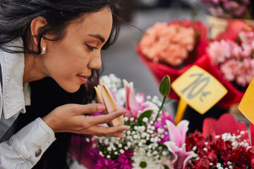 Young Latina woman delighting in the fragrant beauty of colorful flowers at a street vendor's stall.