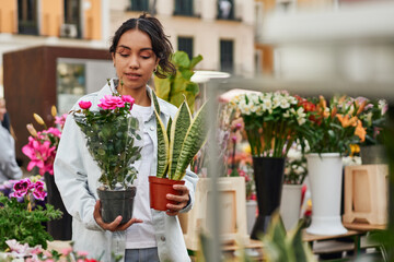 Young Latina woman smiling while purchasing plants from a street vendor's stall, adding beauty to...