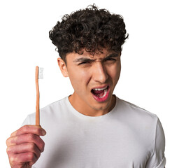 A young latin man brushing with a wooden teethbrush screaming very angry and aggressive.