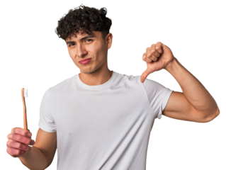 A young latin man brushing with a wooden teethbrush showing a dislike gesture, thumbs down. Disagreement concept.