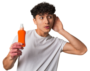 A young latin man holding a solar protection cream trying to listening a gossip.