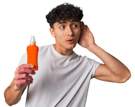 A young latin man holding a solar protection cream trying to listening a gossip.