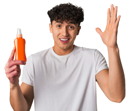 A young latin man holding a solar protection cream receiving a pleasant surprise, excited and raising hands.