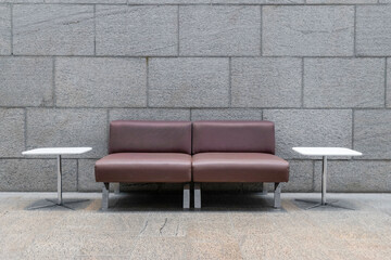 Two armless burgundy leather chairs with aluminum legs, two small white end tables with aluminum legs, marble wall in background, marble floor, nobody