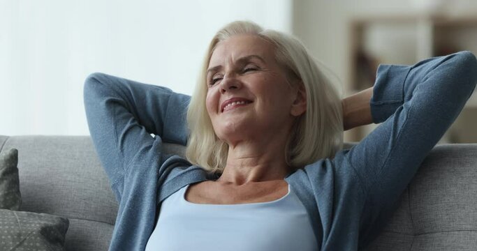 Close up satisfied mature woman resting alone in living room leaned on cozy couch, enjoy accommodation in hotel, spends vacation feels happy, breathing fresh conditioned air in smart home. Relaxation