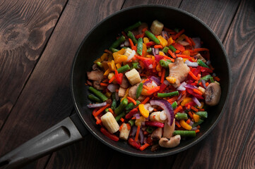 a lot of frozen vegetables in a frying pan on the table. variety of sliced ​​ingredients on a wooden background. juicy fresh vegetables. cooking concept