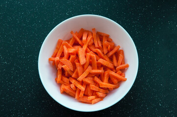 sliced ​​carrots in a plate on a dark background. juicy vegetables in a white bowl on a black...