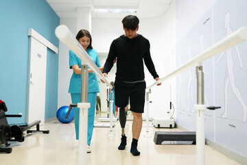 Female physiotherapist helping young man with prosthetic leg..Nurse helping man walk with prosthetic leg..Young disabled man using orthopedic equipment to walk