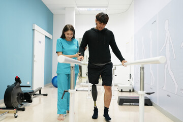 Female physiotherapist helping young man with prosthetic leg..Nurse helping man walk with prosthetic leg..Young disabled man using orthopedic equipment to walk