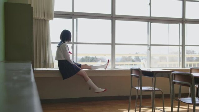 教室の窓際に座る女子高生
