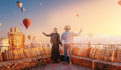 Happy lover couple man and women on rooftop of cave house enjoying of Goreme city panorama,...