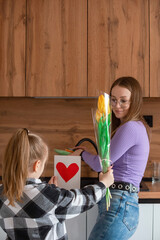 Daughter congratulates mom on Mother's Day, card with heart and flowers. A woman washes dishes and is busy with household chores.