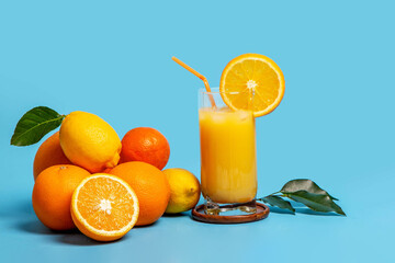 Citrus fruits and a glass of fresh juice on a blue background.