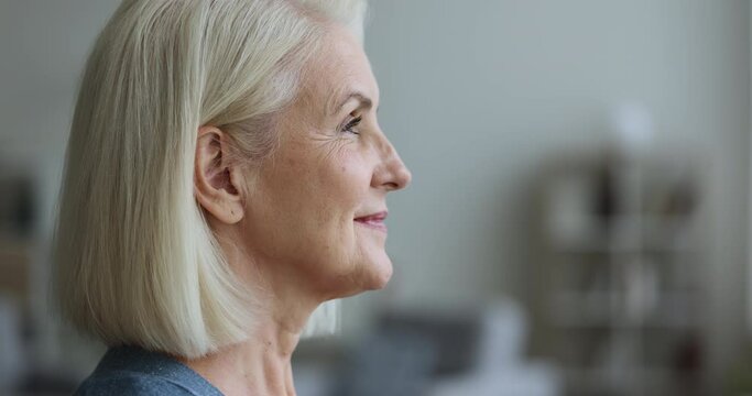 Close up side profile face view mature woman raise head open her eyes smile looks straight, enjoy, welcomes new day, feel happy, enjoy carefree untroubled retired life pose indoor. Eyesight and vision