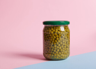 Glass can with green peas on a bicolor pink and blue background. Still life.