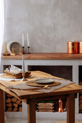 Kitchen utensils, cutlery and candles lie on an authentic wooden table against a blurred rustic kitchen background.