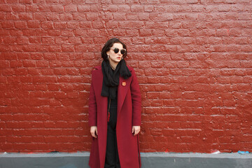 young stylish woman in red coat near red brick wall