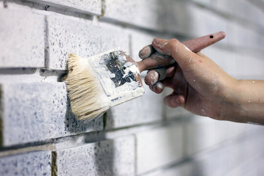 Stock photo of a woman's hand painting a wall white.