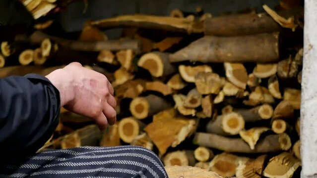 A male baker squatting prepares firewood for a firebox traditional oven. The baker's hands take dry firewood and put it exactly in a pile under a brick oven. Italian pizzeria