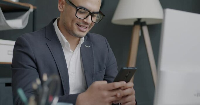 Portrait of businessman texting with smartphone touching screen and smiling getting good news in office. Electronics and businesspeople concept.