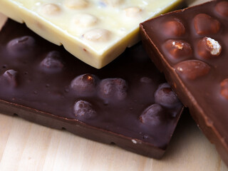 A close-up shot of three chocolate bars with hazelnuts - milk chocolate, dark chocolate and white chocolate on a wooden background.