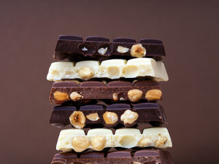 Stack of half chocolate bars with hazelnuts - milk chocolate, dark chocolate and white chocolate on brown background.