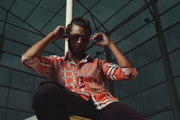 A man wearing a red and white shirt and black pants sits on a ledge.