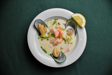 Mussels with king prawns in a creamy sauce with avocado and red fish in a white deep plate on a dark green background
