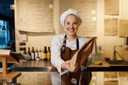 Portrait of friendly smiling bakery seller giving eco package with pastry