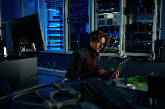 Male system administrator working in server room using laptop