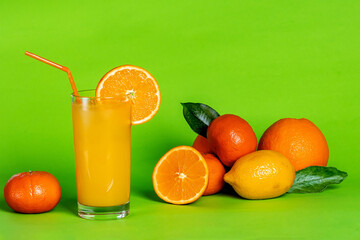 Orange juice in a glass and citrus fruits on a green background