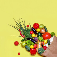 Set of fresh vegetables in a paper bag on a yellow background.