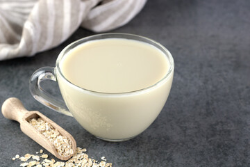 Transparent glass mug of oat milk and oatmeal on a gray background. The concept of alternative lactose-free dairy products.
