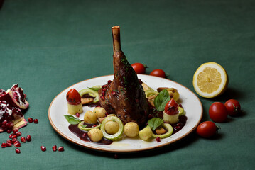 Roasted duck leg with golden crust, grilled vegetables, potatoes, eggplants, and red cherry tomatoes in a white plate on a dark green background. - Powered by Adobe