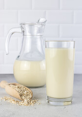 A jug and a glass of oat milk, oatmeal on a white background. The concept of alternative lactose-free dairy products.