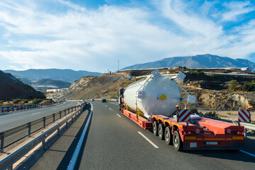 Truck transporting a large tank, on a special trailer for this type of transport, rear view.