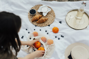 Young woman arranging fruits on the white blanket. Picnic at nature.