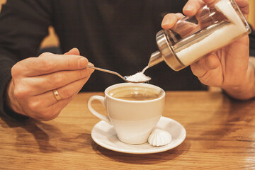 close-up of a businessman's hand with coffee in a cafe, pour sugar to spoon, into a cup of espresso, morning coffee concept.Coffee brake. Morning habit.