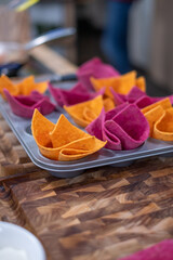 The pink and yellow tortilla baskets with triangular edges in a baking dish on a dark wooden surface. A man in a dark apron in the background. Copyspace