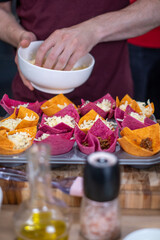 A man adds cheese from a white bowl to the colorful salty baskets. The salt and oil dishes on the table are blurred in the foreground.