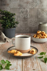 Spring still life on the kitchen table. Ceramic cup of coffee and bowl with homemade puff pastry on a wooden table. Concept for wishing good morning.