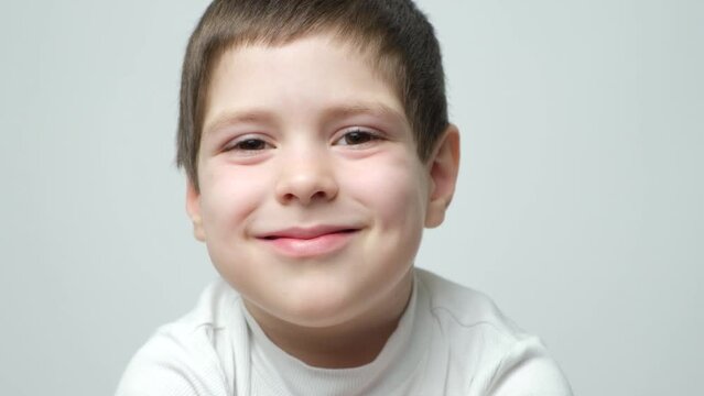 Handsome smart 5 year old brunette boy smiling and staring into the camera, blinking, opening and closing his eyes on a white background