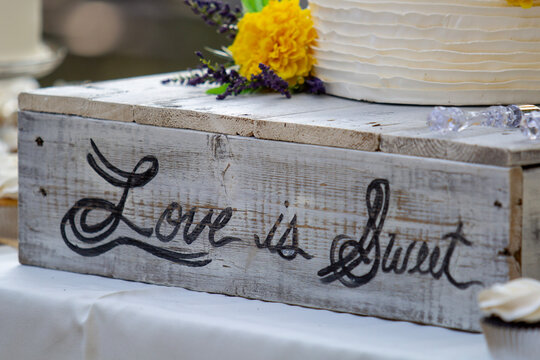 Love is sweet cursive rustic wedding cake stand with yellow flower.