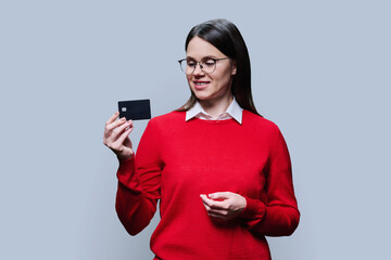 Young woman in red showing bank credit card, on light gray studio background