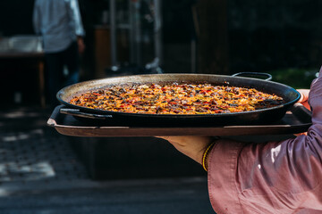 Waiter holding a giant Spanish paella dish outside a restaurant terrace