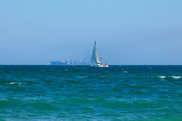 Fototapeta premium Blue Mediterranean Sea, sailing ships with white sailing and big cargo ship.